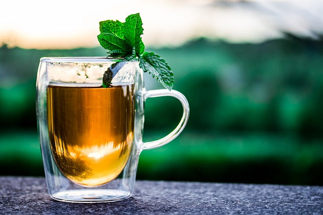 Glas mit blumigem Eistee-Würfel und frischer Minze auf steinerner Oberfläche draußen